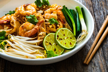 Pad Thai with prawns and rice noodles in peanut and tamarind sauce on wooden table
