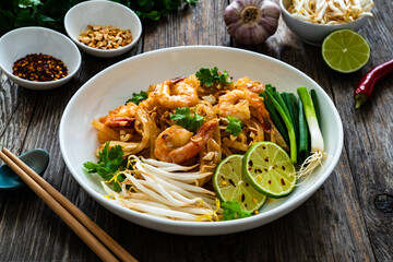 Pad Thai with prawns and rice noodles in peanut and tamarind sauce on wooden table
