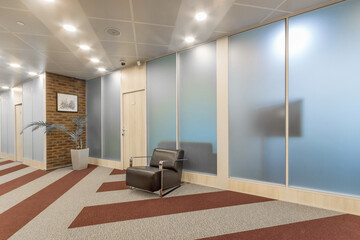 An office reception room with an original floor covering, a glass partition and a black armchair.