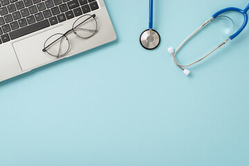 Embrace digital healthcare consultations. Top-down view of a laptop, stethoscope, and glasses set on a soft pastel blue surface with space for your text