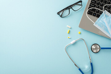Modernize your medical experience online. Top view of a laptop, stethoscope, eyeglasses, pills, and face masks on a pastel blue background, ready for your branding