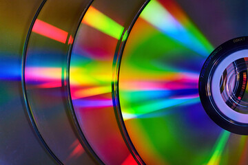 Abstract stack of four silvery CDs with reflective rainbow colored bursts of light on surface