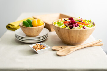 Healthy Vegetable Salad Featuring Bell Pepper and Lettuce in a Bamboo Bowl, Served on a Beige Fabric Tablecloth in a Bright Interior, Accompanied by a Wooden Spoon and White Dishware.