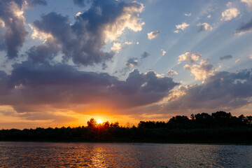Beautiful sky over the river with fluffy blue clouds and orange sun at sunset. Dawn on the lake....