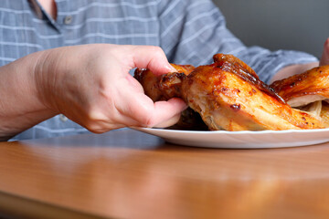 The hands of an elderly woman operate a grilled chicken