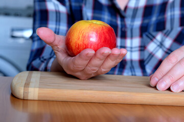 The hands of an elderly woman hold a red ripe tasty juicy apple