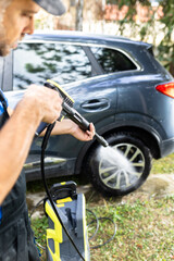 Worker washing or spraying car wheel with high pressure washer outdoors.