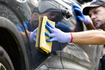 Professional car wash worker in workwear detailing and wiping car with rag outside - obrazy, fototapety, plakaty