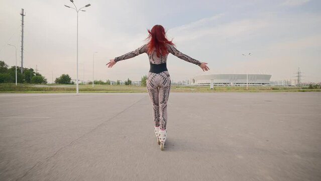 Slim Woman with Red Hair Has Fun Rollerblading on an Asphalt Parking Lot. Happy Girl Roller-Skates and Raises Her Arms to the Sides, Feeling Freedom and Wellbeing. Slow Motion.
