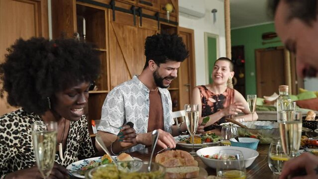 Young and diverse group of friends having a toast with wine while having lunch together in their rented apartment