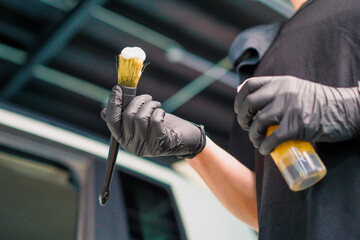 Close-up of a car wash worker applying car wash foam to a brush while washing a luxury car during the detailing process