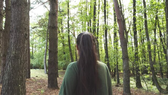 Back view follow shot of young woman wearing a green blouse walking trough forest in early autumn season