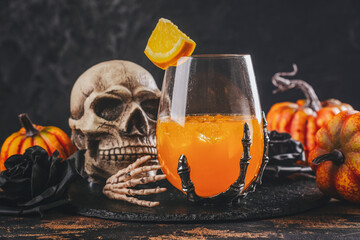 Halloween orange cocktail in spooky skeletons hand glasses