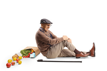 Elderly man with a rocery bag sitting on the floor and holding his leg
