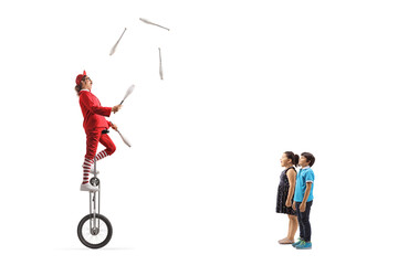 Children watching an acrobat riding a giraffe unicycle and juggling