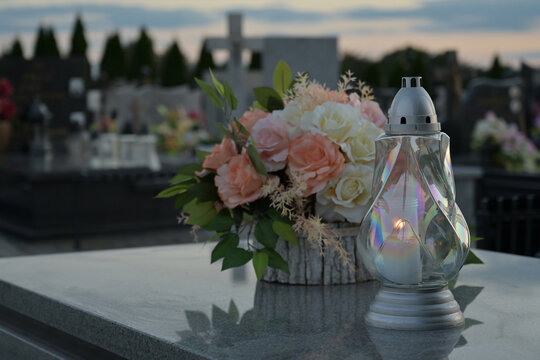 Candle and flowers on the tomb with cemetery in the background.