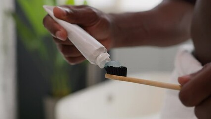 Close up hands squeezing out white toothpaste from tube on toothbrush dental care morning procedure oral hygiene prevent tooth caries unknown African American man prepare brushing teeth in bathroom