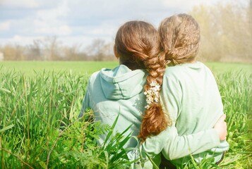 The idea of ​​friendship. Two girls friends are sitting hugging on the green grass, view from...