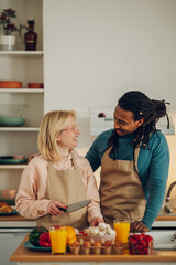 An affectionate married interracial couple hugs and cooks food at home together.