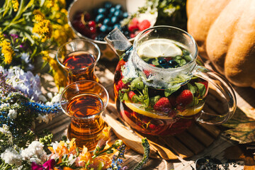 tea with fruits and berries being brewed in a transparent teapot next to flowers and berries on the...