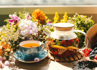 tea with fruits and berries being brewed in a transparent teapot next to flowers and berries on the...