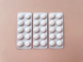 Three whole white rectangular plates with ten small round tablets in each lie side by side in a horizontal row on a white background, close-up, top view. Medicines.