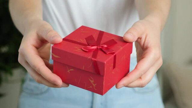 A woman holds out a gift in a red square box. Gift giving concept