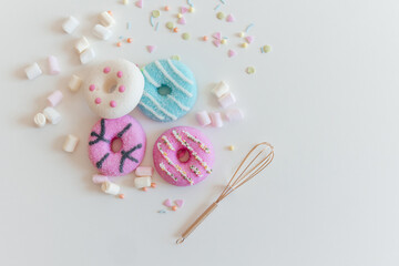 Top view of Marshmallows and Colorful donuts with a golden whisk on white table 