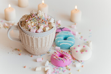 Cup of hot chocolate. Sprinkling chocolate on marshmallows in mug with cocoa. Colorful donuts on a white table surrounded with candles