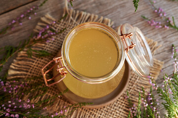 A jar of herbal syrup with fresh heather blossoms