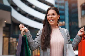 Beautiful young business woman holding shopping bags and showing excitement while standing in front...
