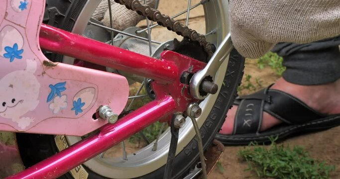 The father repairs the child's pink bicycle and replaces the wheel and chain. A man wearing gloves fixes the small wheel of a child's bicycle into place after repair. DIY bicycle repair concept.