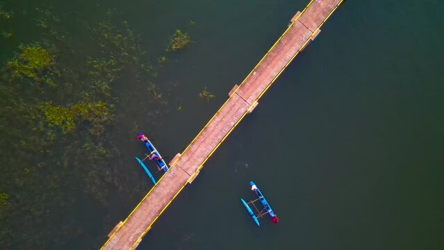 Aerial view of boats passing under a bridge on a large lake, depicting rural fishing boat life in the evening