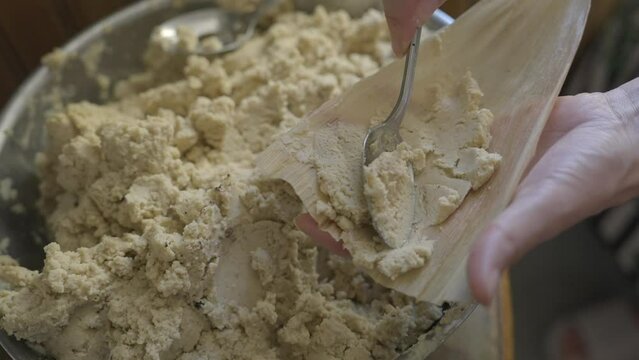 This close up video shows hands making tamales and putting masa on corn husks.