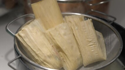 This video shows hands places tamales in a pot steamer. - Powered by Adobe