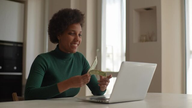 Cheerful African-American young woman showing on video call dollars cash won in lottery or casino. Concept of lending, success and winning. Successful black female happy show the income, slow motion.