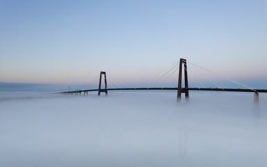 Tranquil, blue-sky scene featuring the Hale Boggs Memorial Bridge shrouded in foggy mist