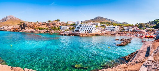 Scenic beach situated along the shoreline of a tranquil bay in Cala Sant Vicenc, Spain - obrazy, fototapety, plakaty