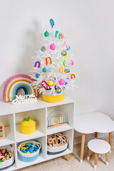 Children's room with littel white christmas tree decorated bright and colorful decorations, rainbow, balls and toys. Merry Christmas and Happy Holidays!