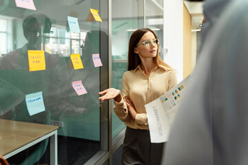 Businesswoman wearing stylish eyeglasses using sticky notes, agile methodology for productivity