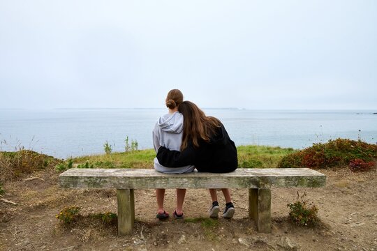 Rear view of two young female friends sitting on a beachside bench