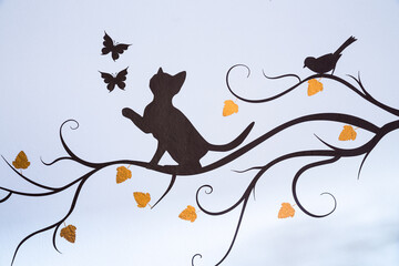 Cat playing with butterflies on a branch with yellow autumn leaves and a bird