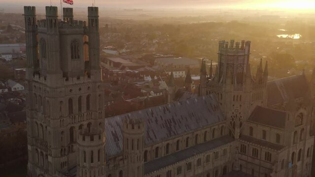 Scenic aerial view Ely cathedral tower with british flag on post beautiful morning sunrise light. Cambridgeshire. Holy and undivided Trinity Anglican cathedral in UK
