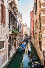 Fototapeta na wymiar Row of small boats is moored along a picturesque canal in a bustling cityscape in Venice, Italy