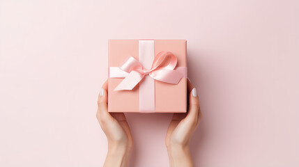 Female hands handling a gift box wrapped in light pastel colors. Small gift box with elegant ribbon tied in a bow, background with copy space, top view. 