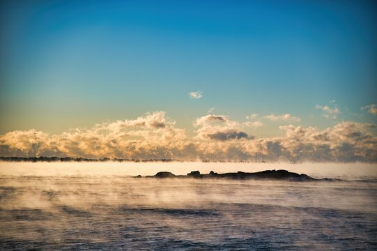 Sea smoke hovers over the Thames River with a cloudy sky backdrop