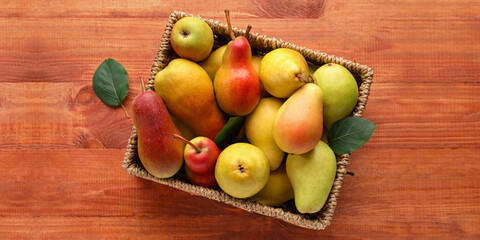 Wicker box with ripe pears on wooden background, top view