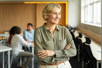 Portrait of smiling middle aged businesswoman, manager with crossed arms working in modern office