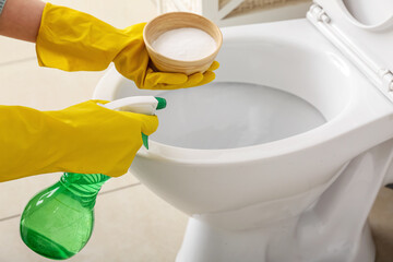 Woman in rubber gloves cleaning toilet bowl with baking soda and sprayer, closeup