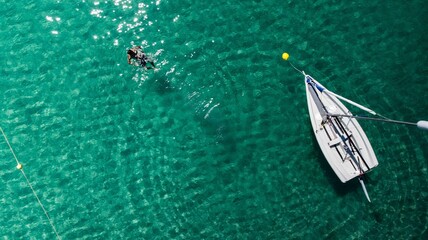 Small sailboat and a person are in the center of a tranquil body of water in the Greek island